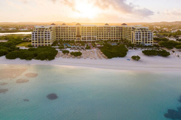 A large hotel with multiple floors and a central courtyard, surrounded by lush greenery and a beach. - The Ritz-Carlton, Aruba (Noord)