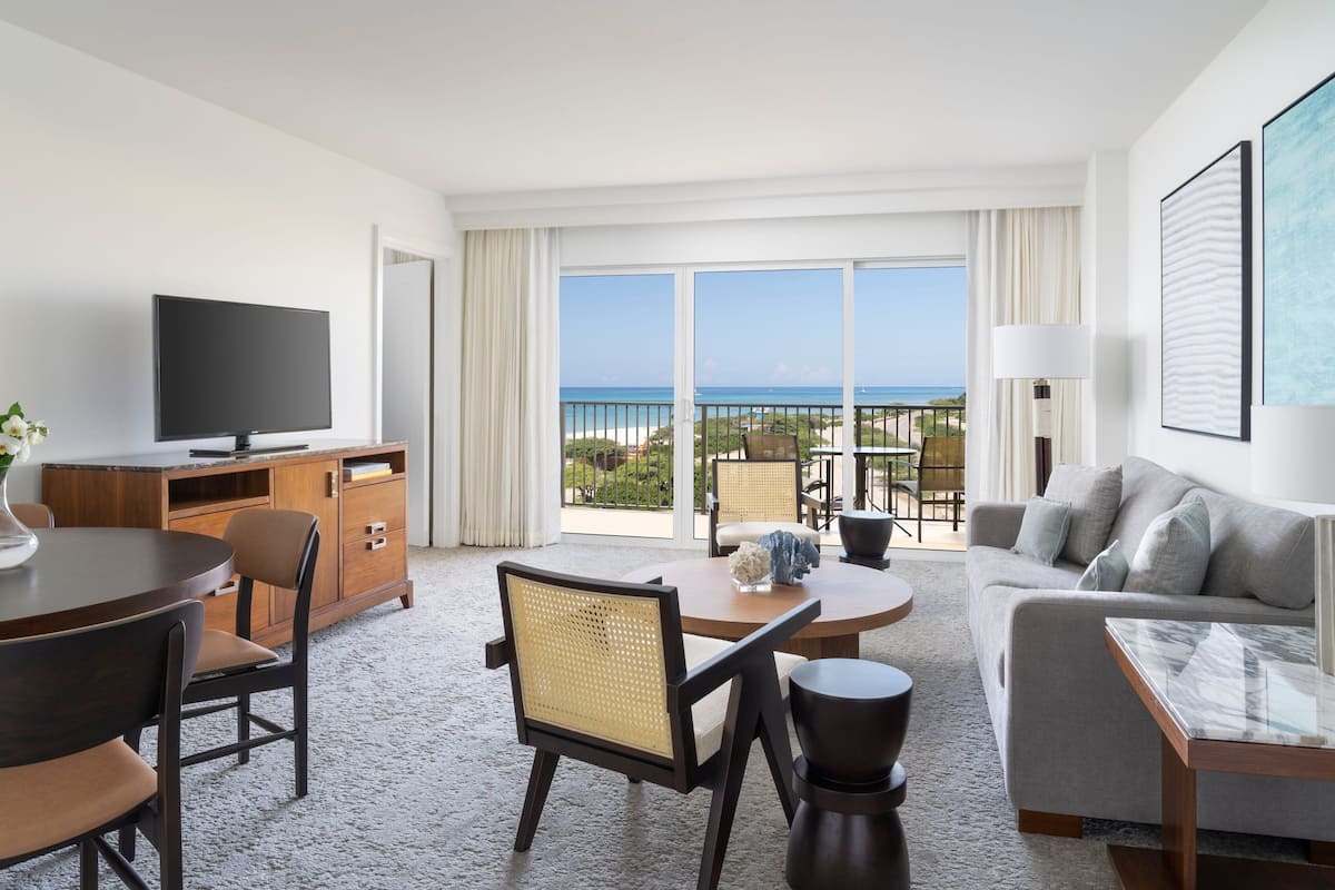 Una habitación de hotel con balcón, televisión de pantalla plana, zona de comedor con mesa y sillas, y un sofá.