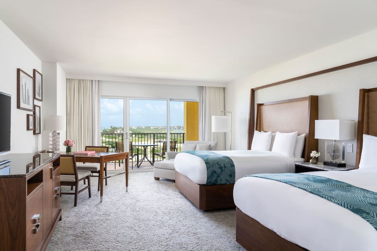 Habitación de hotel con dos camas, un escritorio, una silla, un televisor y un balcón con vistas.
