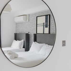 A hotel room with a bed, pillows, a towel, a wall-mounted air conditioner, and a framed abstract artwork. - Camden Town Hotel (London)