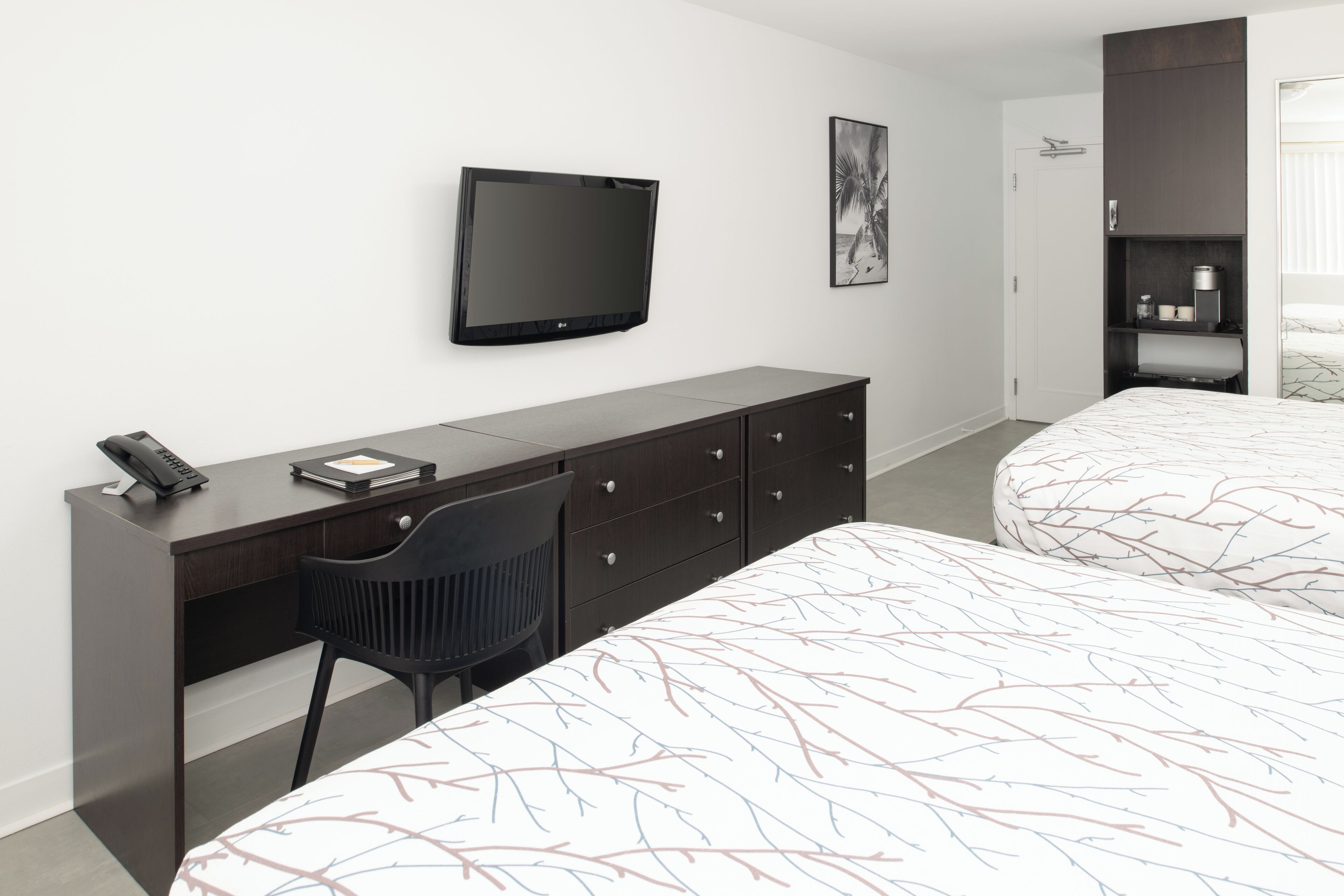 Una habitación de hotel moderna con escritorio, silla, cama, televisor y armario.