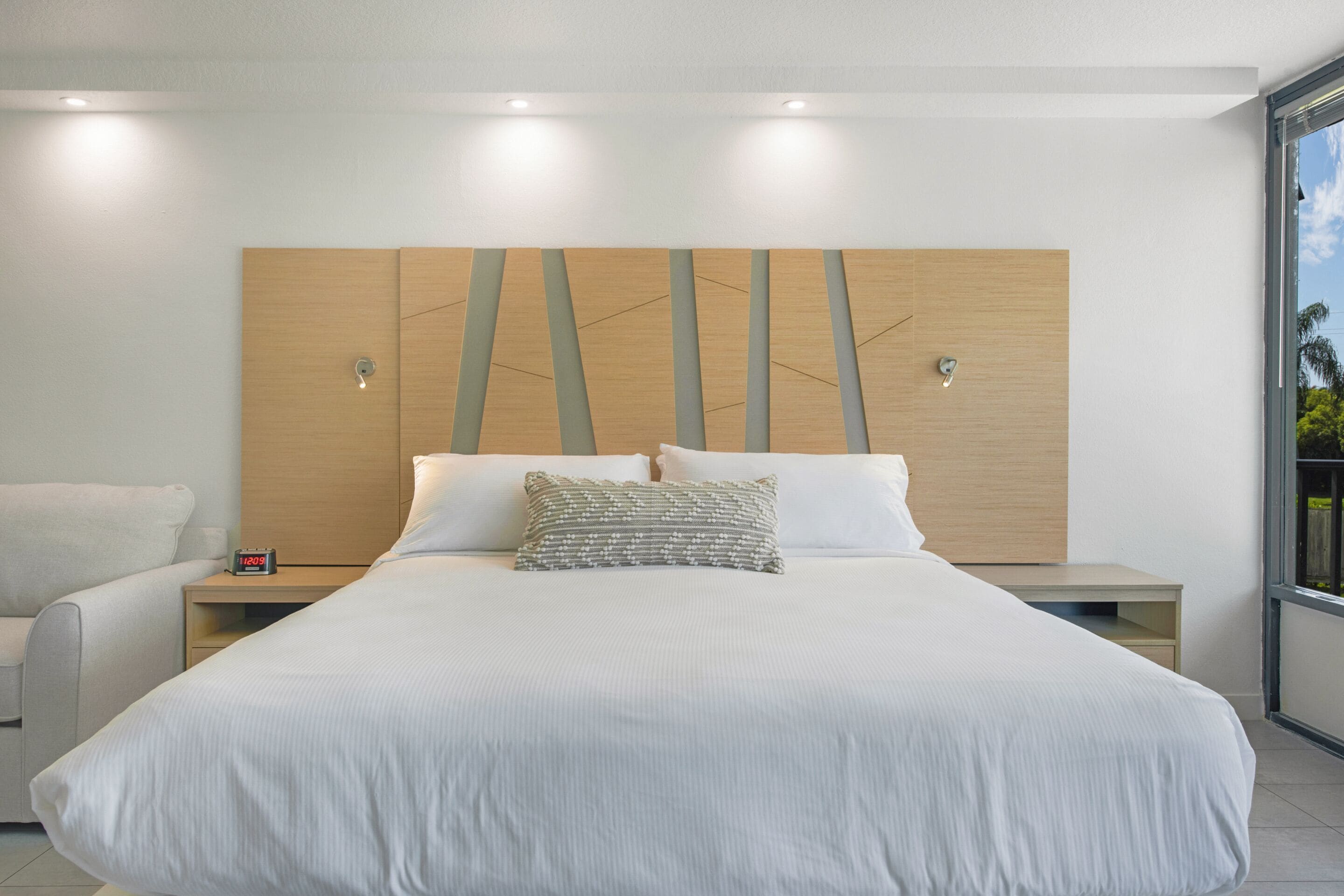 Une chambre moderne avec un grand lit, deux tables de chevet, une commode et une vue sur l’extérieur.