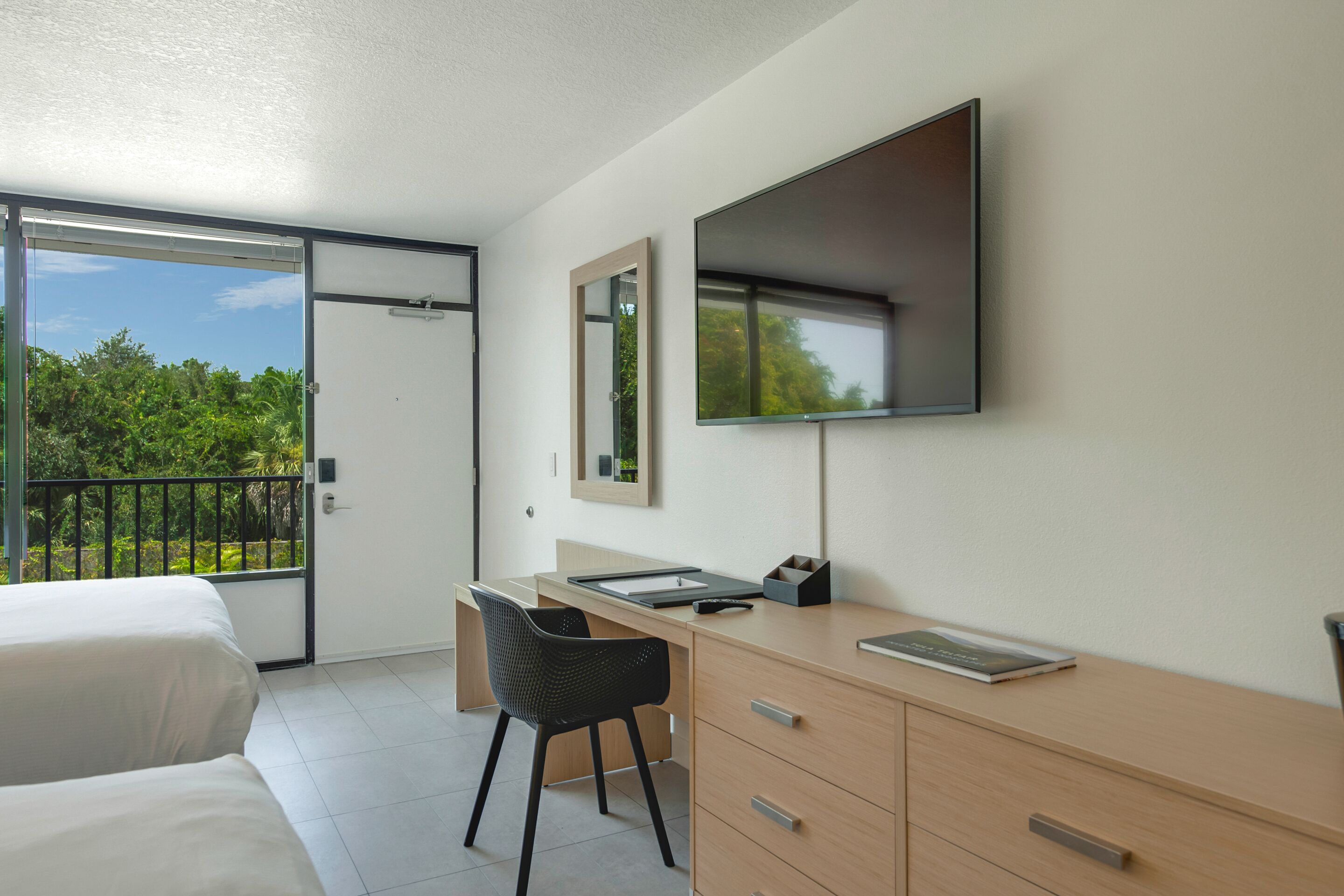 Une chambre d’hôtel équipée d’un lit, d’un bureau, d’une chaise, d’une télévision et d’un balcon donnant sur un paysage verdoyant.