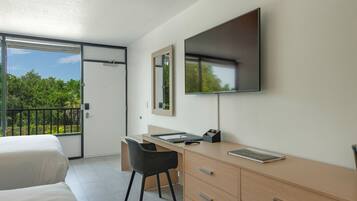 Une chambre d’hôtel équipée d’un lit, d’un bureau, d’une chaise, d’une télévision et d’un balcon donnant sur un paysage verdoyant.