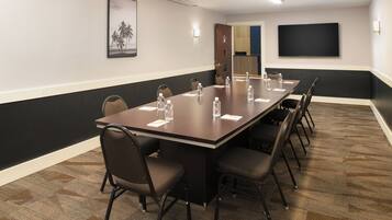 Een vergaderzaal met een lange tafel, stoelen, waterflesjes en een televisiescherm.