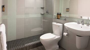 Un baño moderno con ducha de vidrio, inodoro blanco y lavamanos con espejo.