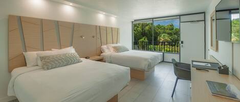 A modern hotel room with two beds, a desk, and a balcony with a view of greenery.