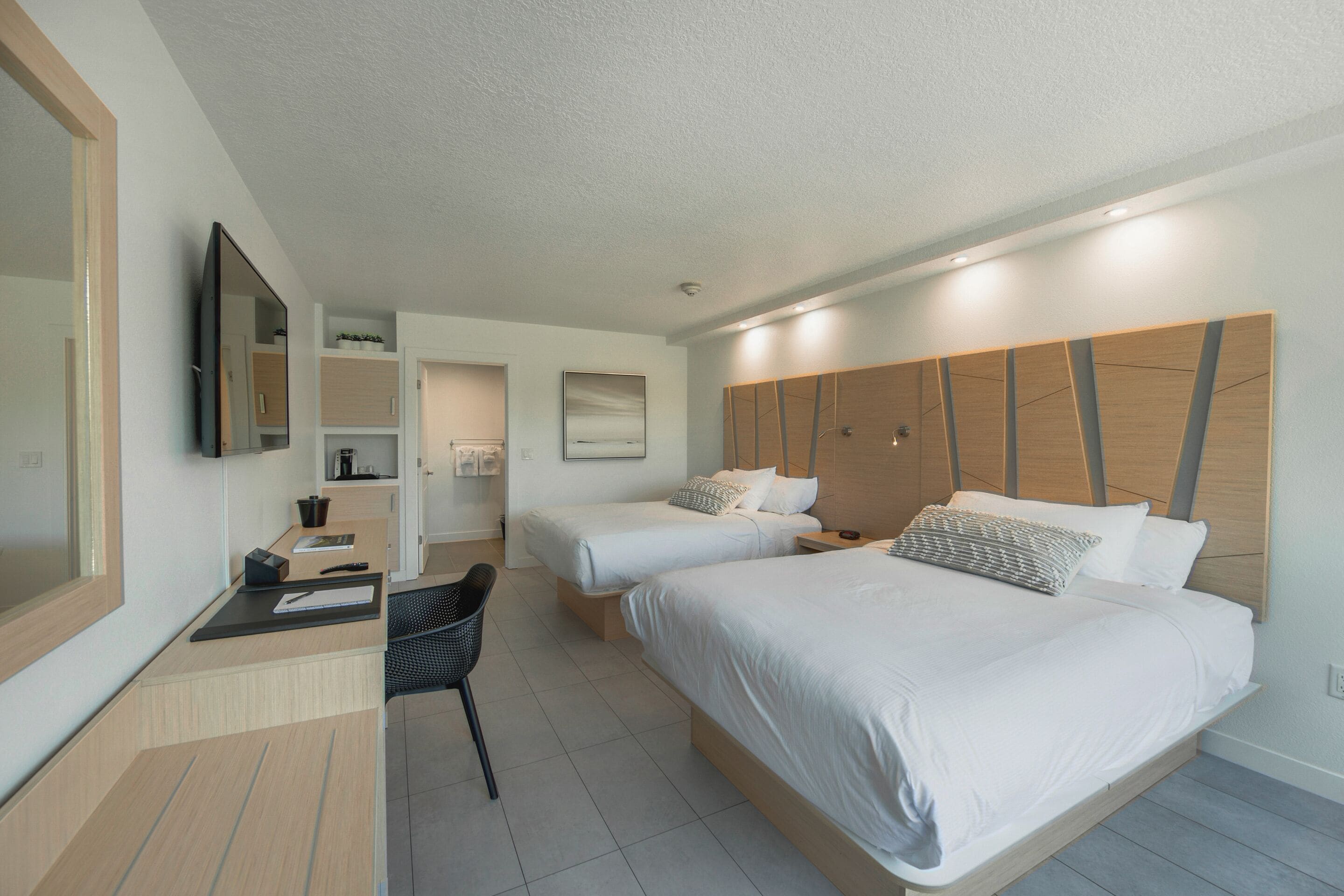 Quarto de hotel moderno com duas camas, uma escrivaninha e uma cadeira.