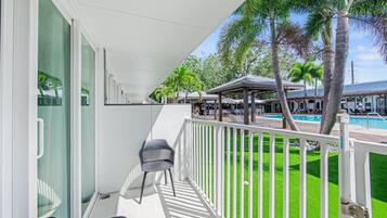 A balcony with a white railing, a black chair, and a view of a swimming pool and palm trees.