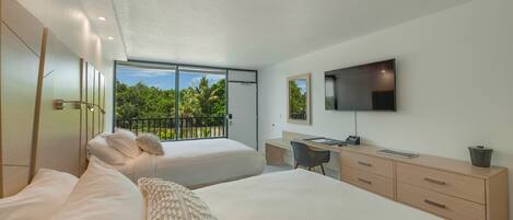 Une chambre moderne avec deux lits, un bureau, une chaise, une télévision et un balcon donnant sur un espace verdoyant.