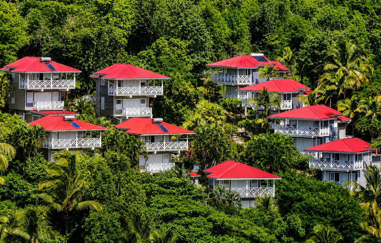 Un conjunto de edificios con tejados rojos y balcones blancos, rodeado de frondosa vegetación verde.