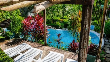 A wooden deck with white lounge chairs, a pool, and lush tropical plants.