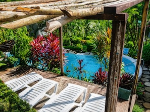 A wooden deck with white lounge chairs, a pool, and lush tropical plants.