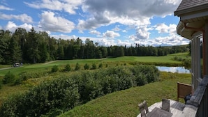 Vista de un campo de golf con un estanque, rodeado de árboles y un edificio con porche.