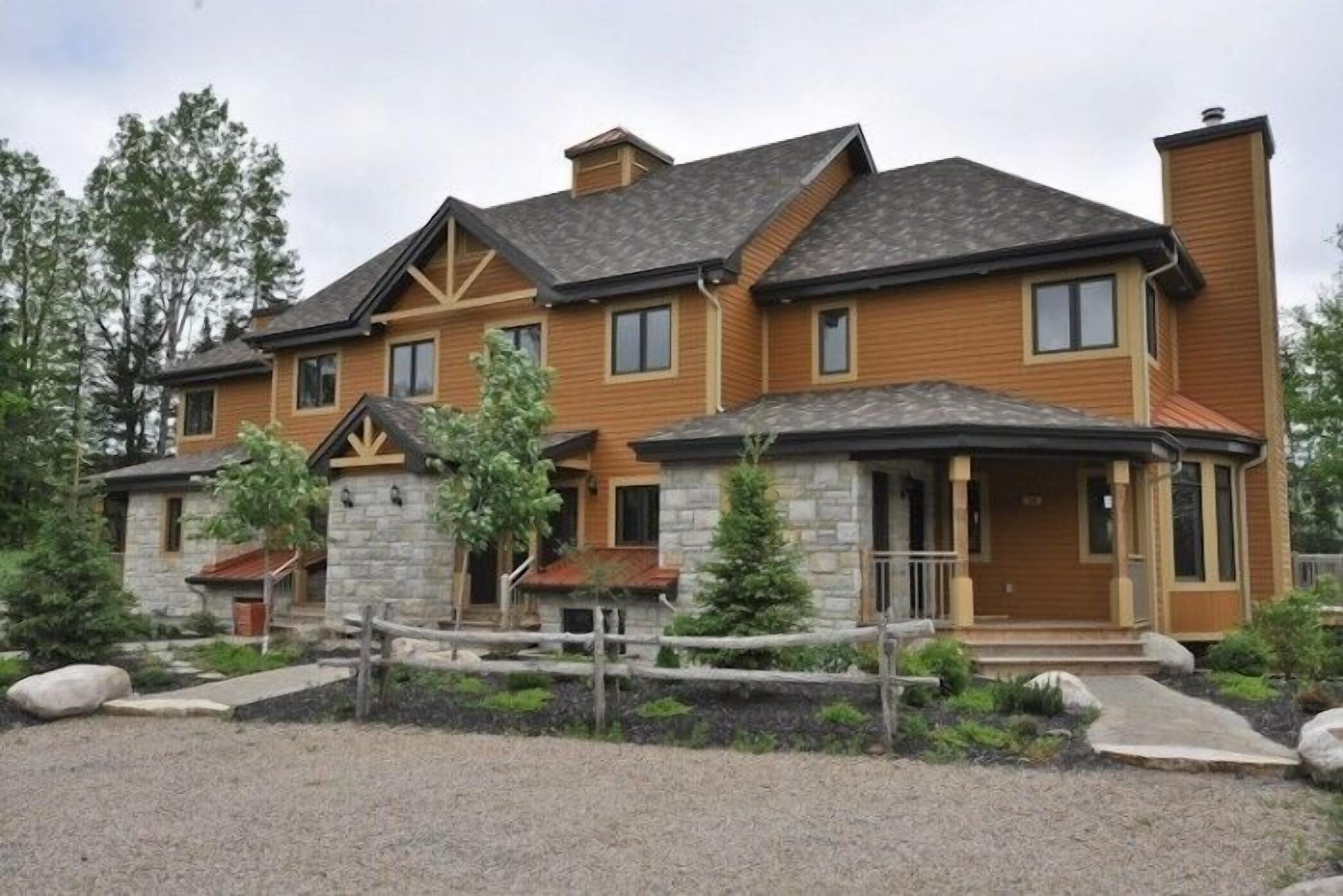 A two-story house with a stone foundation and wooden siding, featuring a front porch and a fenced yard.