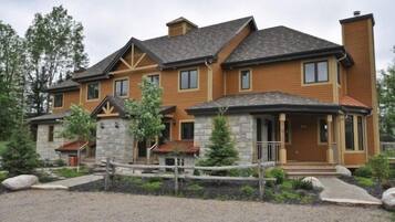 A two-story house with a stone foundation and wooden siding, featuring a front porch and a fenced yard.