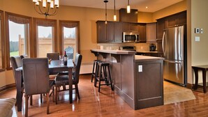 Una cocina moderna con gabinetes de madera oscura, electrodomésticos de acero inoxidable, una isla central con taburetes y una lámpara de araña.