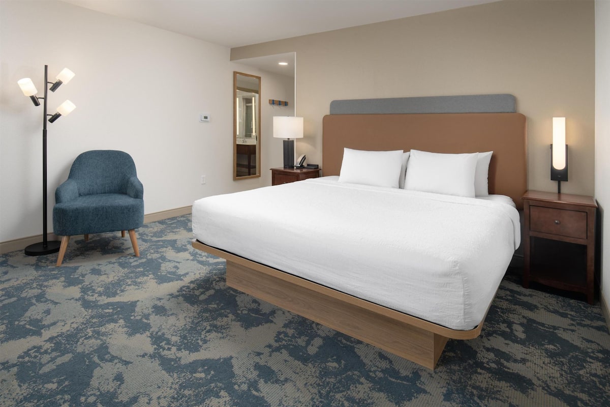 A hotel room with a large bed, a chair, a nightstand, a lamp, and a floor lamp.