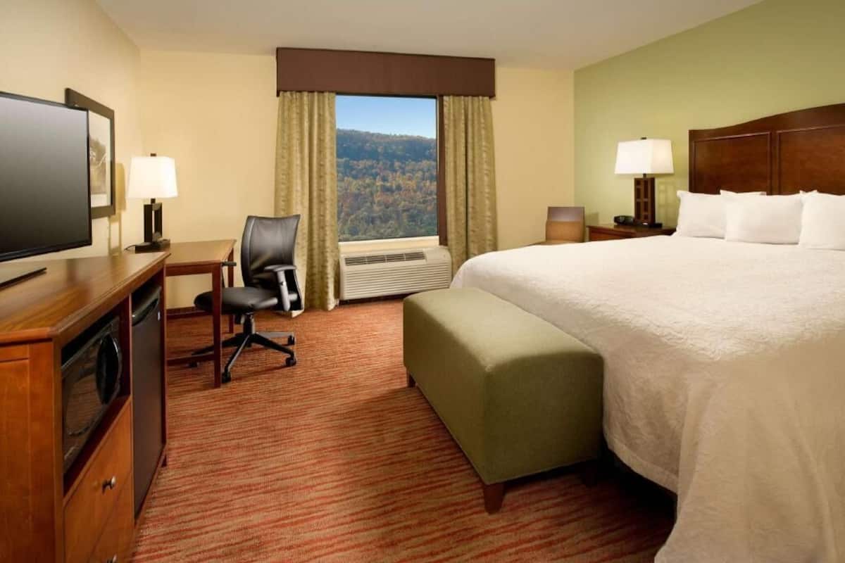 A hotel room with a bed, a desk with a computer, a chair, a TV, and a window with curtains.