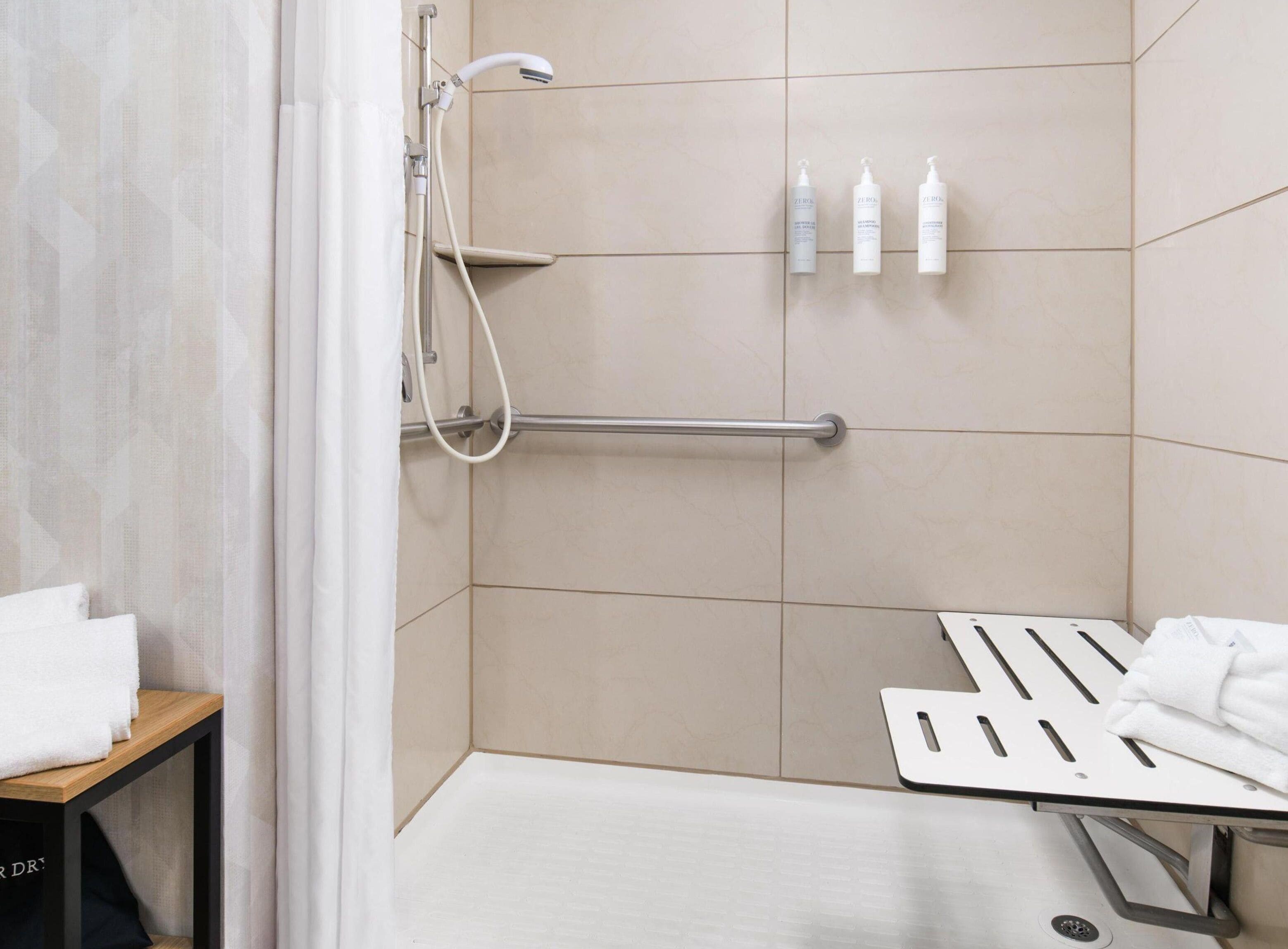 Un espace douche équipé d’une barre d’appui, de trois bouteilles de shampoing et d’un porte-serviettes.