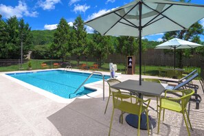 A swimming pool with a sunshade, outdoor seating, and a fenced area with trees in the background.