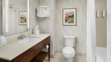 Un baño con lavamanos doble, inodoro, cortina de ducha y dos cuadros en la pared.