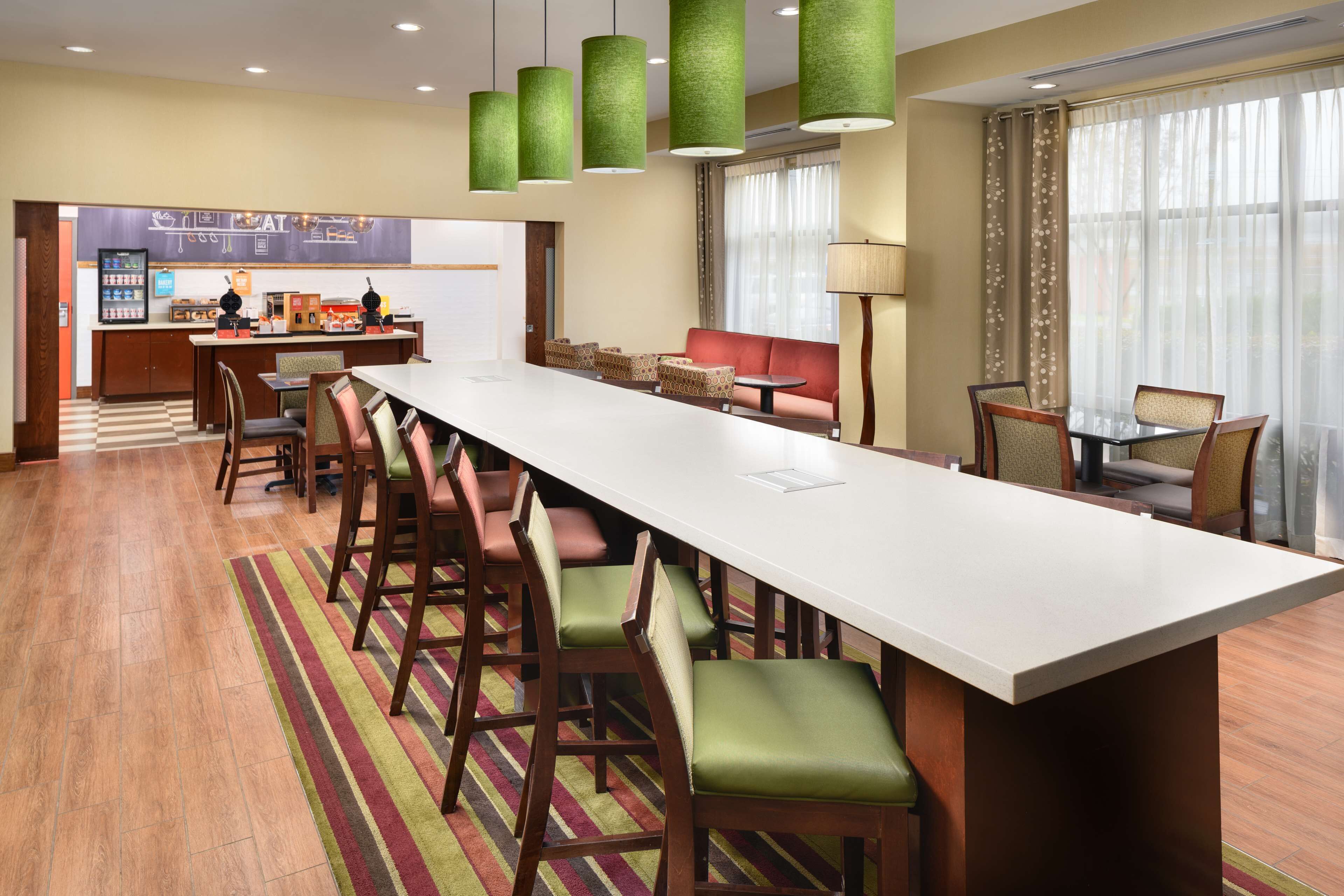 Un vestíbulo de hotel con una larga barra, taburetes, un sofá y un comedor.