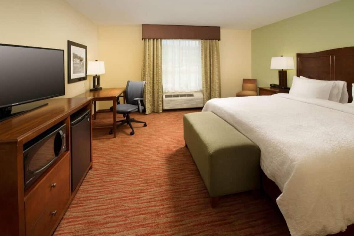 A hotel room with a bed, desk, chair, television, and a window with curtains.