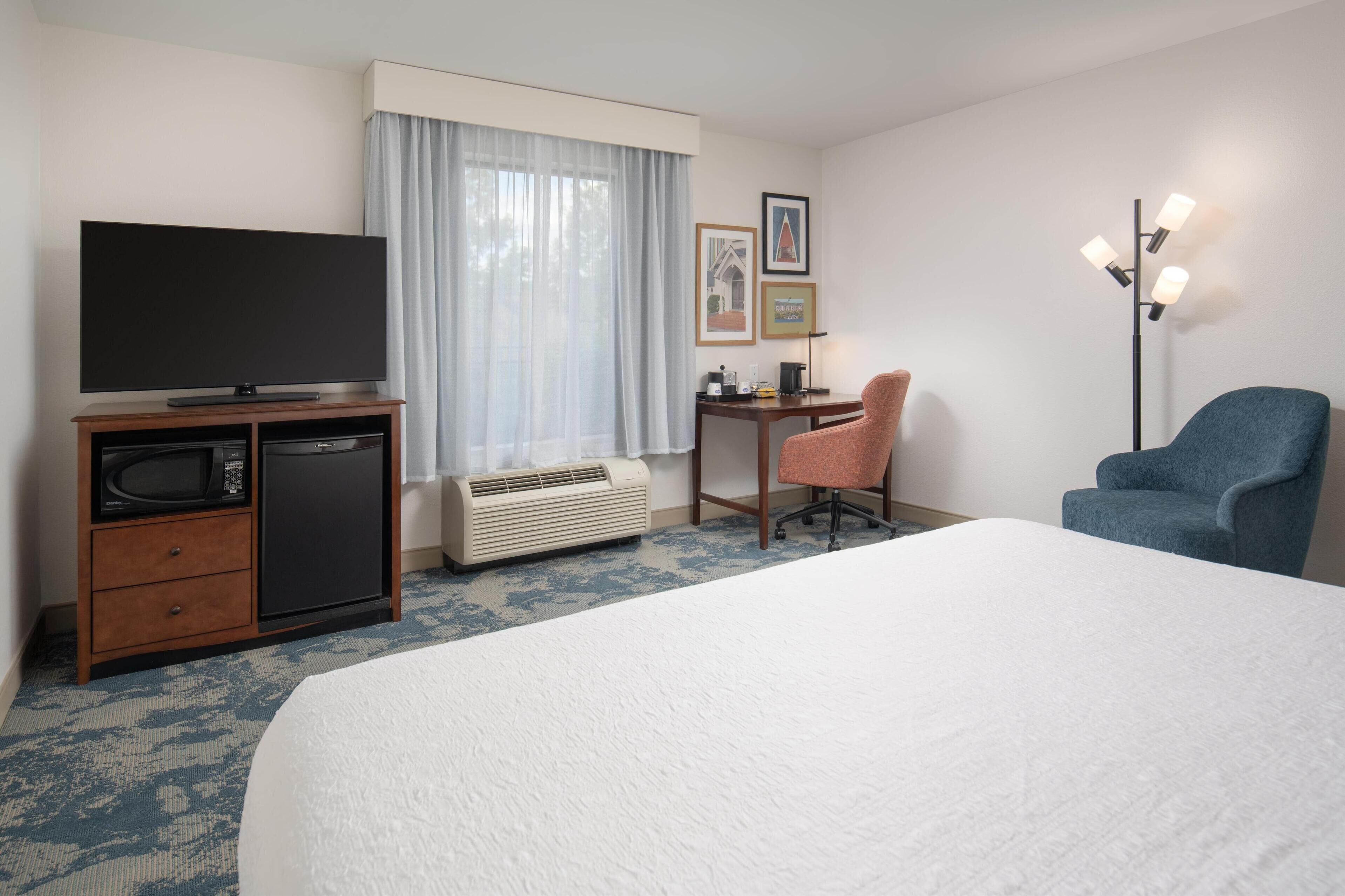 Una habitación de hotel con cama, escritorio, televisor, silla y calentador.