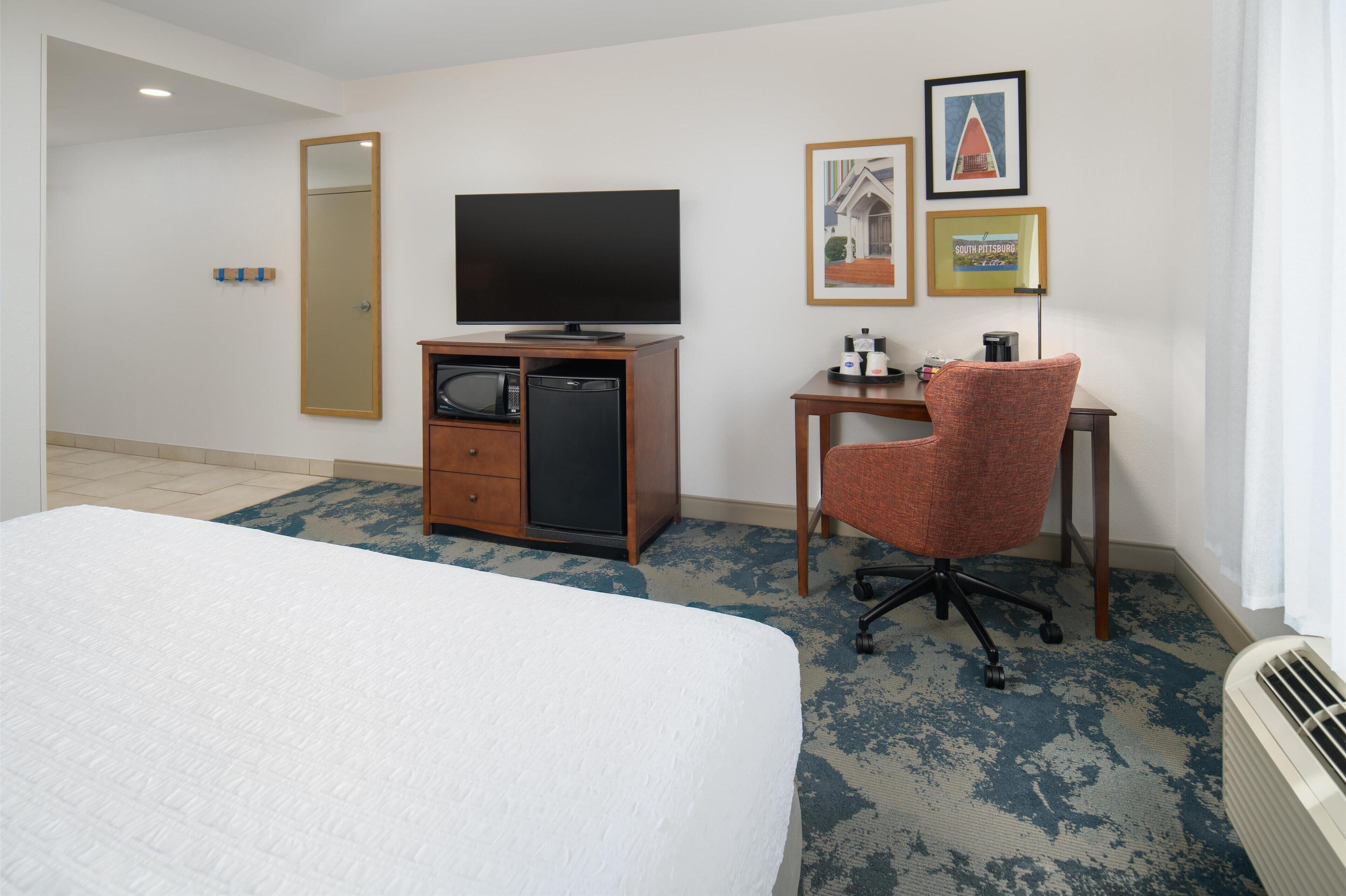 A hotel room with a bed, a desk, a television, a microwave, and framed pictures on the wall.