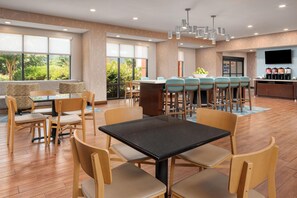 A modern dining area with a mix of tables and bar seating, large windows, and a flat-screen TV on the wall. - Hampton Inn Kimball (Jasper)