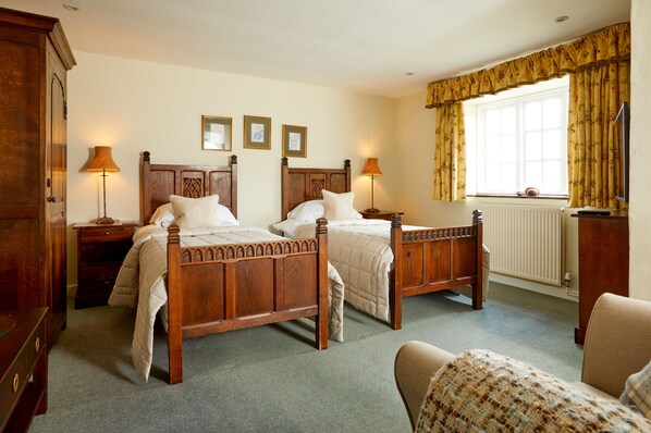 A traditional bedroom with two wooden beds, a radiator, and a window with curtains. - Burford House (Burford)