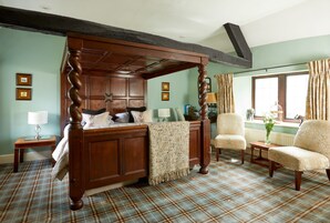 Un dormitorio tradicional con cama con dosel, dos sillones, una mesita y una ventana con cortinas.