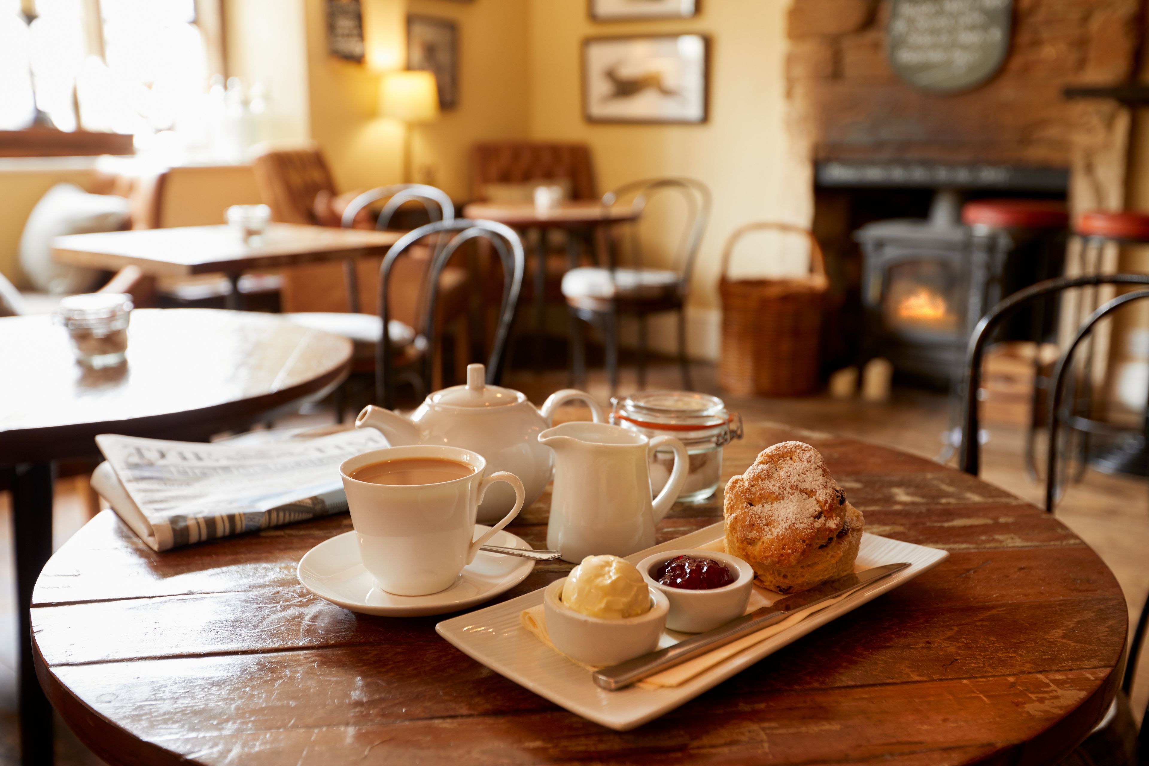 A cozy cafe setting with a table set for tea and pastries, including a scone, jam, and a small bowl of cream.