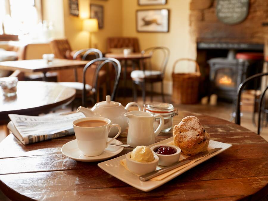 A cozy cafe setting with a table set for tea and pastries, including a scone, jam, and a small bowl of cream.
