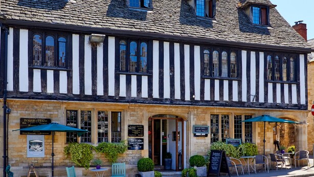 A traditional Tudor-style building with a black and white timber-framed facade, multiple windows, and a welcoming outdoor seating area with tables and chairs. - Burford House (Burford)