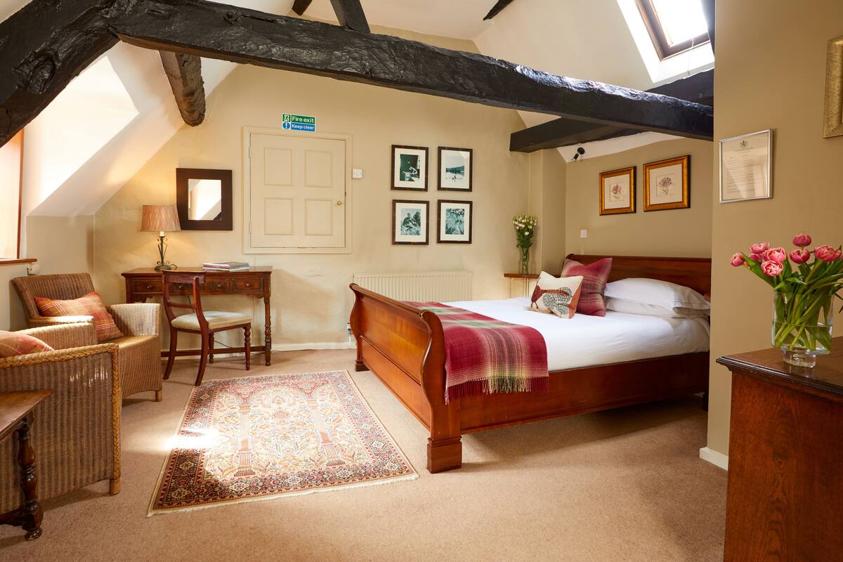A bedroom with a wooden bed, a desk, a chair, and a large window.