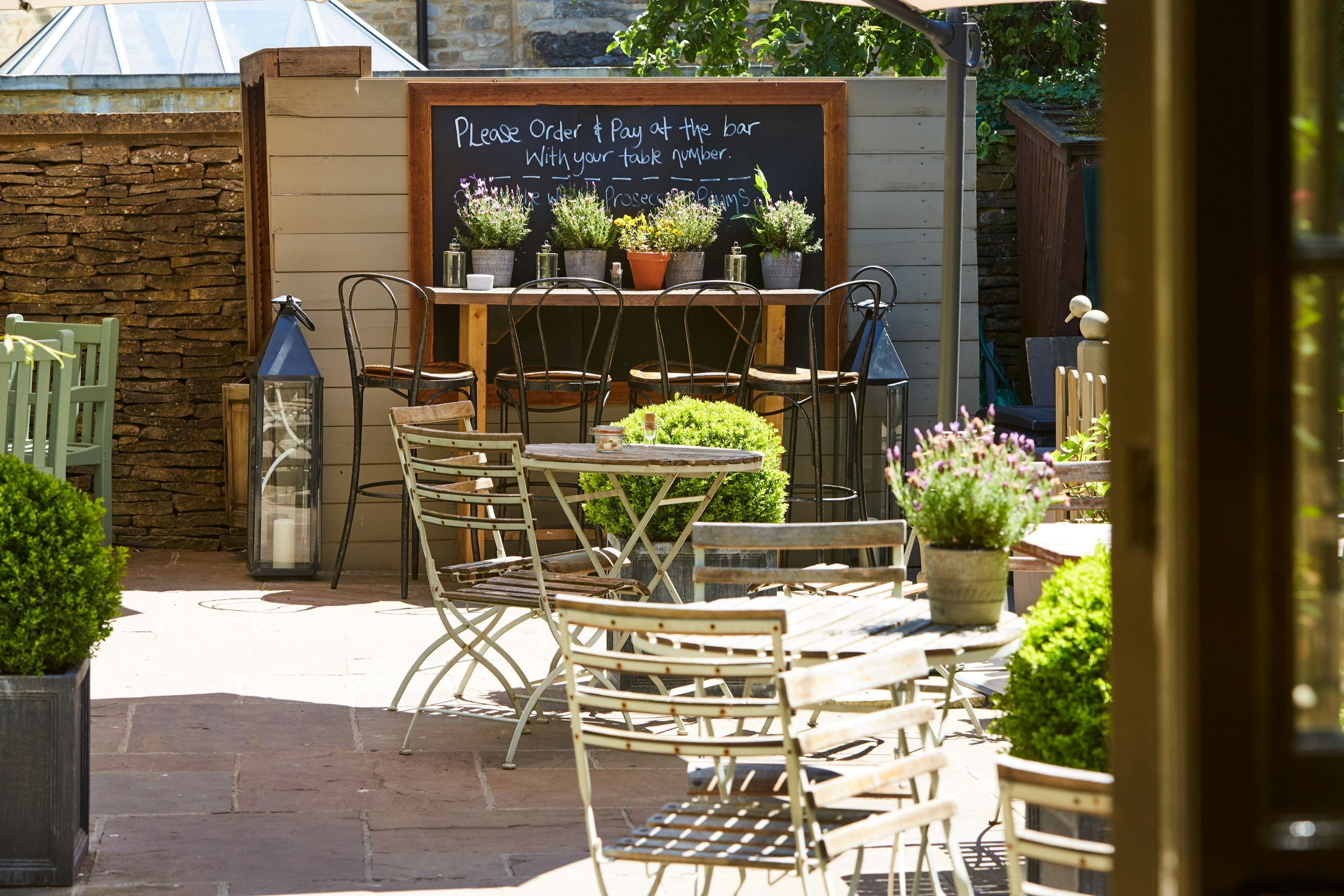 An outdoor café with tables and chairs, a chalkboard sign, and potted plants.