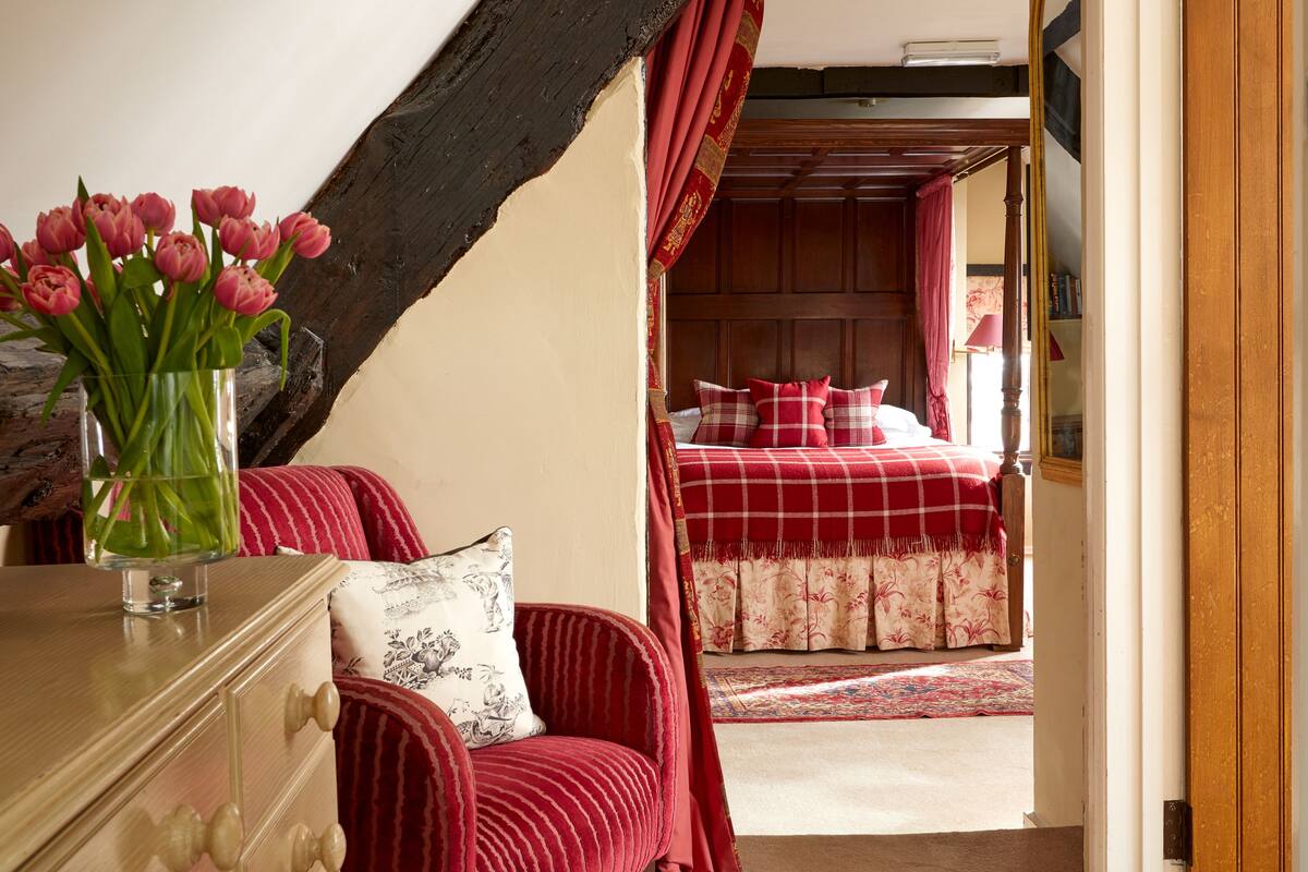 A bedroom with a red checkered bedspread, a wooden headboard, and a red and white striped chair.