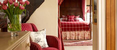 A bedroom with a red checkered bedspread, a wooden headboard, and a red and white striped chair.
