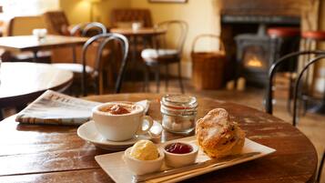 A cozy dining area with a round wooden table, a cup of coffee, a pastry, and a small bowl of jam.
