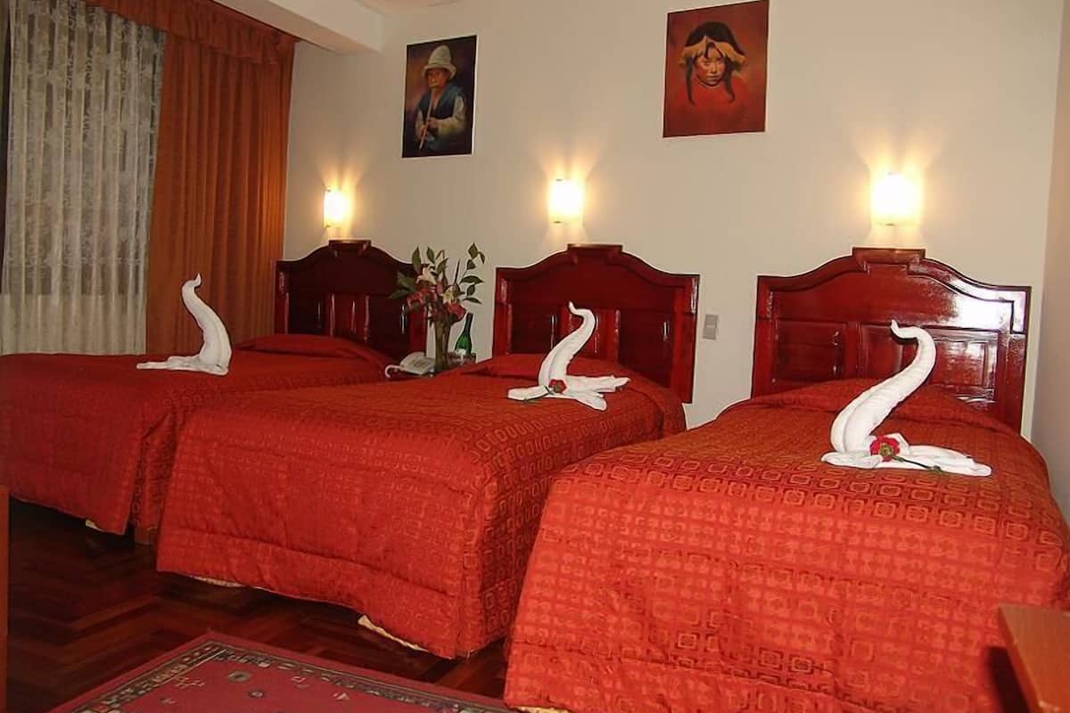 A hotel room with two beds, each with a swan-shaped towel, red bedding, and a wooden headboard. There are wall-mounted lights and a painting above the beds.