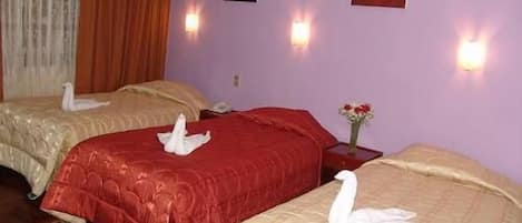 A hotel room with two beds, each with a swan-shaped pillow, a red bedspread, and a beige bedspread. There are wall-mounted lights and a vase with flowers on a nightstand.