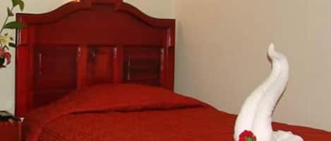 Una cama bien hecha con una colcha roja y una escultura de toalla blanca con una rosa.
