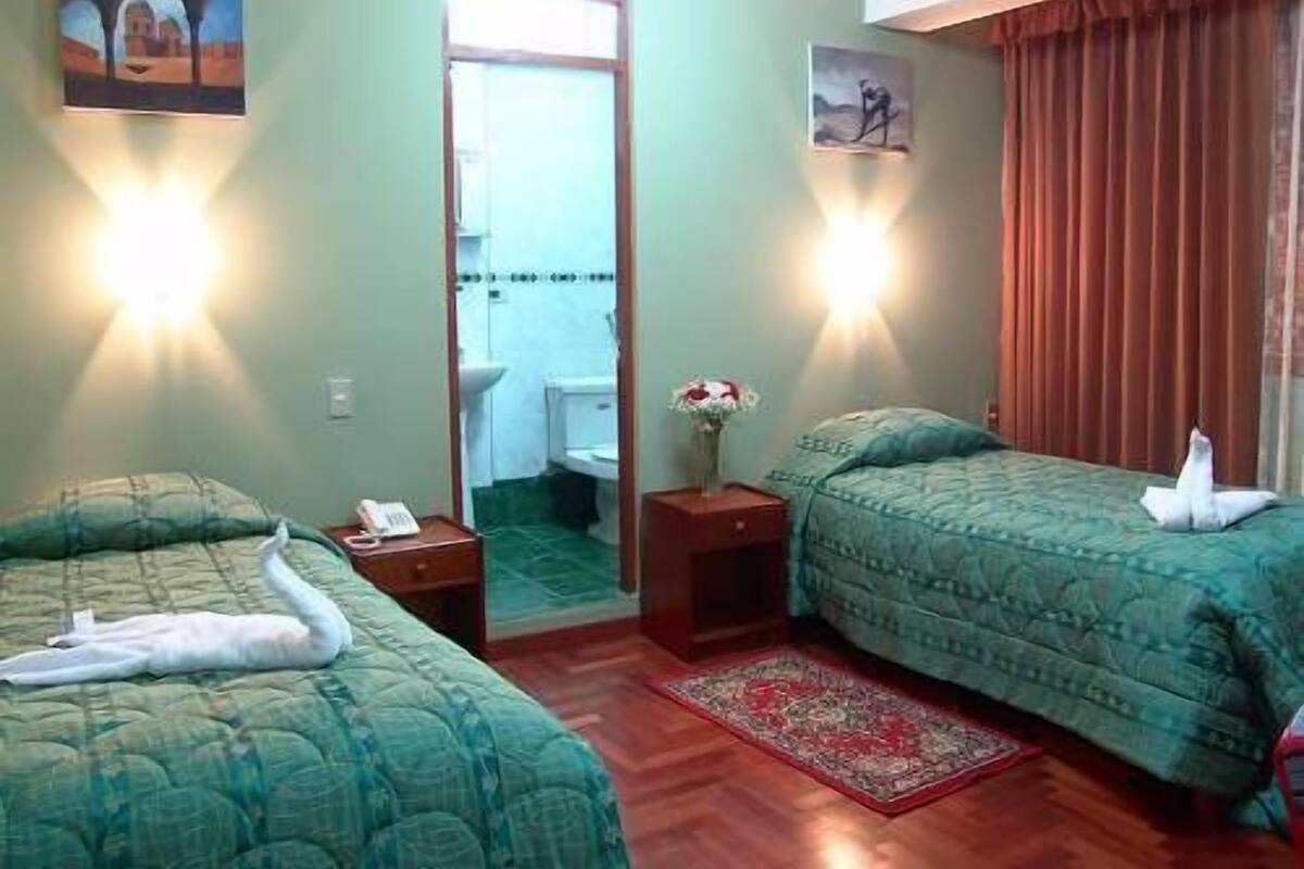 A hotel room with two beds, a mirror, a small table with a phone, a vase with flowers, and a red rug.