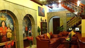 A lobby with a large mural, a staircase, leather sofas, and a coffee table. - Inkayra Hotel (Cusco)