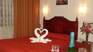 A hotel room with a red bedspread, a wooden headboard, two wall sconces, a bouquet of flowers, a bottle of champagne, and two glasses on the nightstand. - Inkayra Hotel (Cusco)