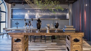 A dining area with a long wooden table, decorative vases, and a large abstract painting on the wall.