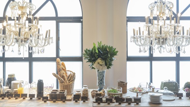 A buffet setup with a variety of food items, a vase of flowers, and a chandelier.