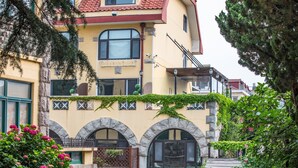 A two-story building with a yellow facade, stone arches, and a balcony with a wrought iron railing.